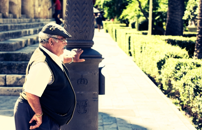 Un om în vârstă din Sevilla, sprijinindu-se de un stâlp într-o zi fierbinte de vară.