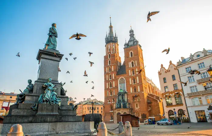Old city center view with Adam Mickiewicz monument, St. Mary's Basilica and birds flying in Krakow on the morning