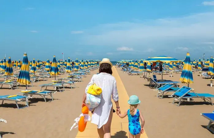 Woman and child outdoors. Mother and daughter going to rest on beach. Rimini, Italy.