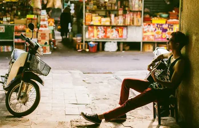 asian artist man plays guitar with bike and market background