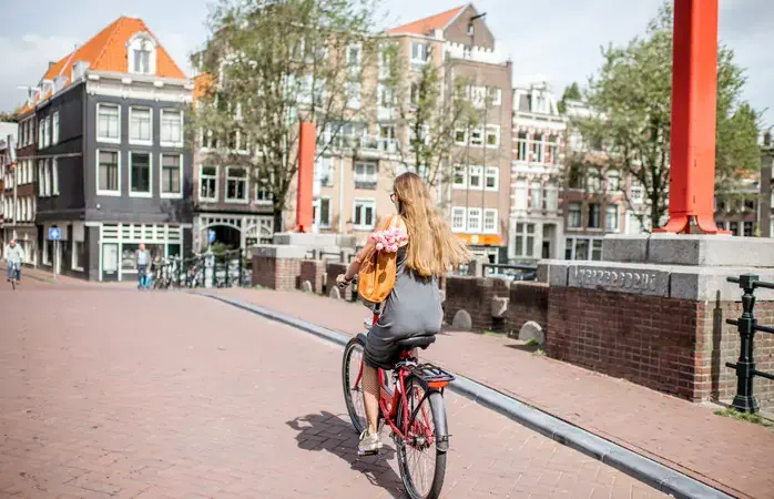 Young beautiful woman riding a bicycle with bag and bouquet of tulips on the bridge over the water channel in Amsterdam old city